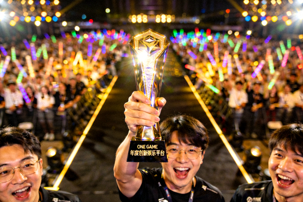 ONE GAME团队代表在颁奖典礼舞台上高举年度创新娱乐平台奖杯，背景是璀璨的灯光和热烈的观众